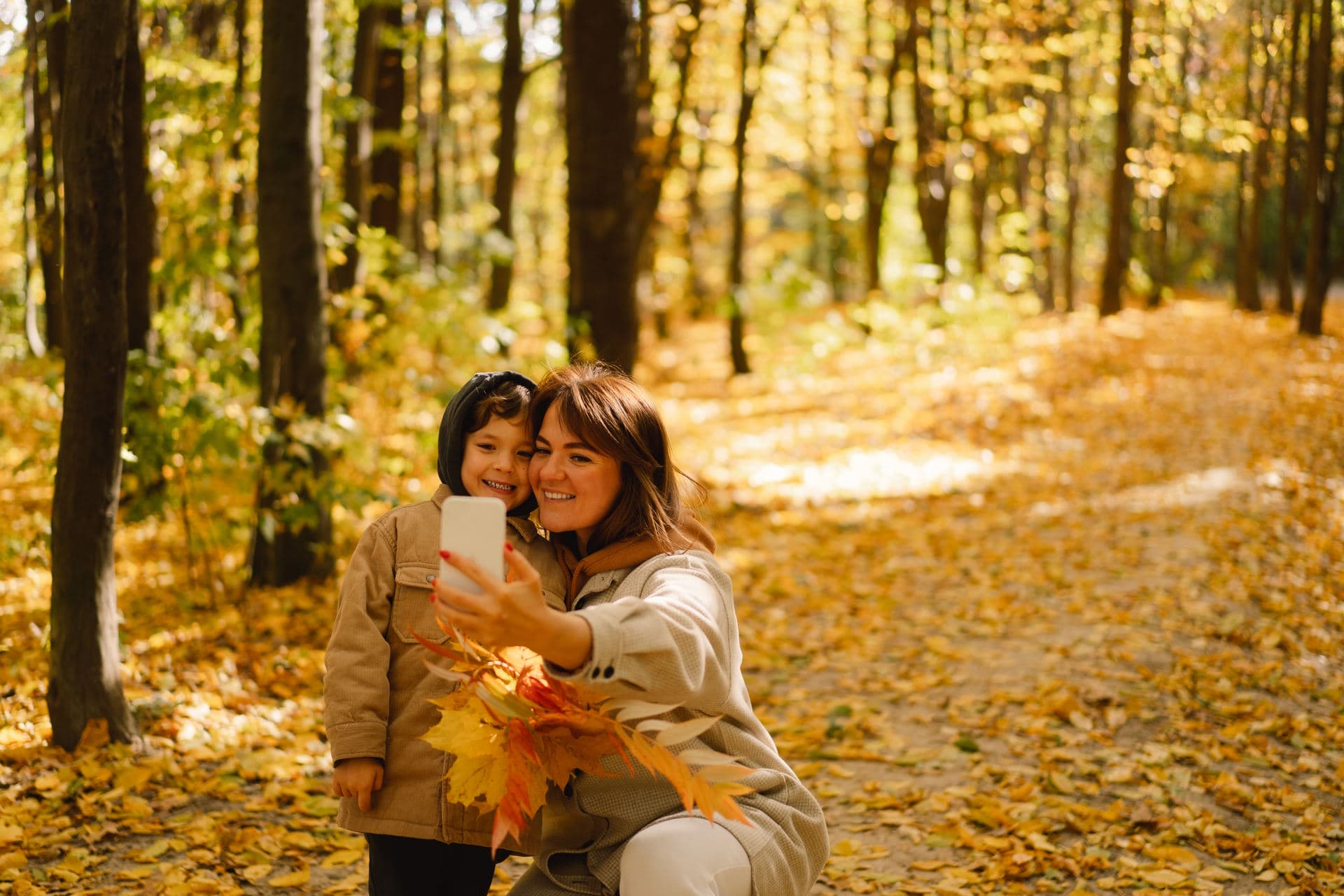 Mom and son take a selfie on the phone in the autumn forest. People use technology. Autumn outdoor activity for family with kids. Happy mother's day. Family day. Autumn day. Happy family leisure.